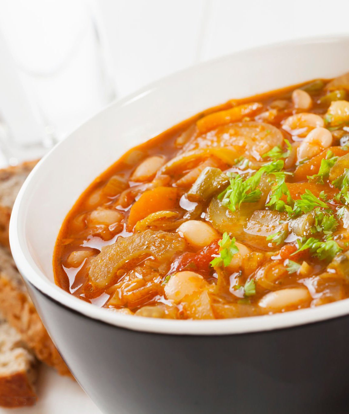 A bowl of vegetable soup on a table with bread.