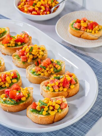 bruschetta recipe with canned corn and juicy tomatoes with a bright base of basil pesto on garlic-toasted bread.